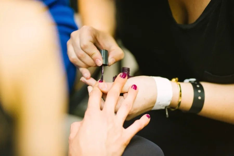 Manicure aplicando esmalte nas unhas de uma cliente